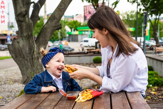 Hübsche junge Mutter und Tochter, die einen großen Burger in einem Café essen