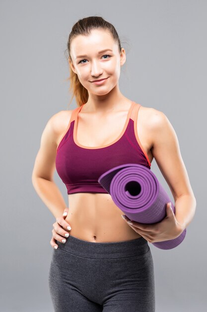 Hübsche junge Sportlerin, die Fitnessmatte hält, während sie isoliert steht