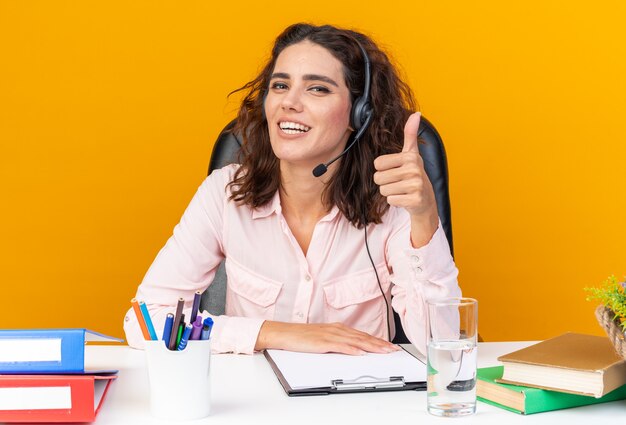 Hübsche kaukasische Callcenter-Betreiberin mit Kopfhörern, die mit Bürowerkzeugen am Schreibtisch sitzen