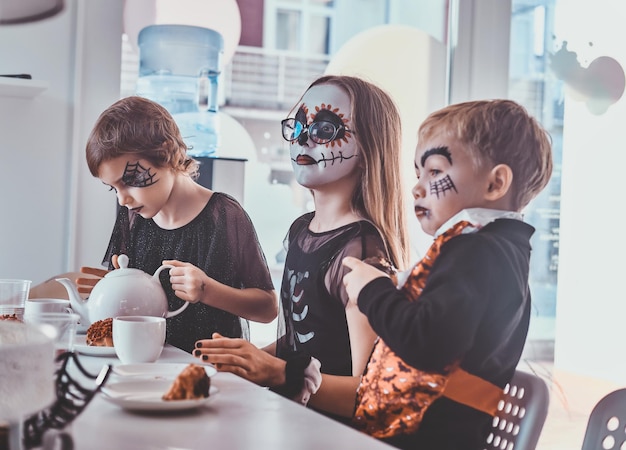 Hübsche Kinder in gruseligen Halloween-Kostümen veranstalten eine festliche Party mit leckerem Essen und Süßigkeiten.