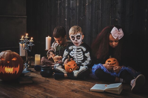 Hübsche kleine Kinder in Halloween-Kostümen genießen die Party, während sie ein Buch lesen.