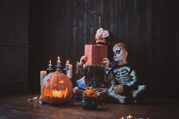 Hübsche kleine Kinder in Halloween-Kostümen genießen die Party, während sie ein Buch lesen.