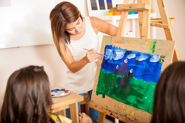 Hübsche Kunstlehrerin, die einer Schülerin beim Malen im Kunstunterricht hilft