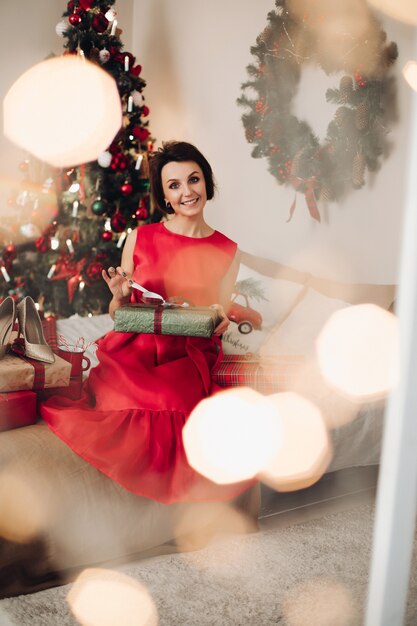 Hübsche lächelnde Frau, die in ihrem Schlafzimmer mit Weihnachtsgeschenk sitzt