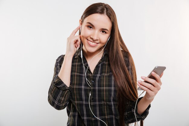 Hübsche lächelnde Frau im Hemd, die Musik hört