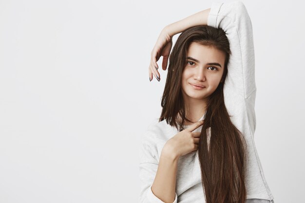 Hübsche lächelnde freudige Teenagerfrau mit dunklen langen Haaren, die drinnen posiert, lässig gekleidet.