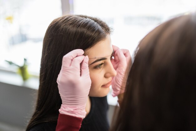 Hübsche Meisterin in weißen Handschuhen bestimmt die Augenbrauenkontur des jungen Modells