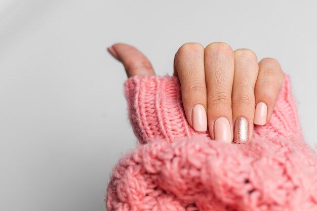 Hübsche nackte Farbmaniküre, ein Finger glänzend golden, auf gestricktem rosa Wollpilloverhintergrund