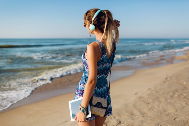 Hübsche reisende frau, die musik am strand hört