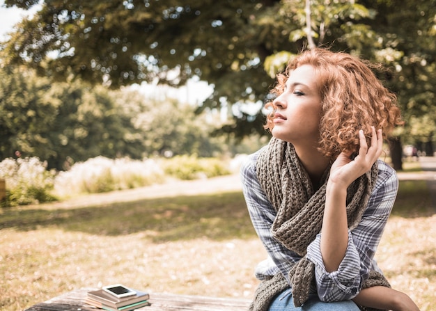 Kostenloses Foto hübsche rothaarigefrau, die auf bank im park sitzt