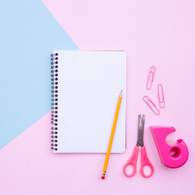 Hübsche Schreibtischzusammensetzung mit Notizbuch und Bleistift und Scheren auf hellblauem und rosa Hintergrund