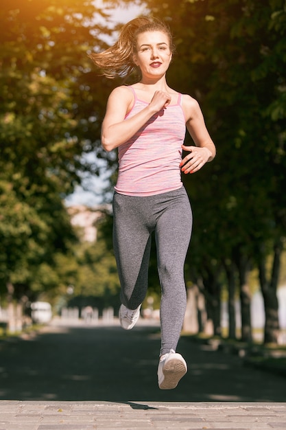 Kostenloses Foto hübsche sportliche frau, die im park im sonnenaufganglicht joggt