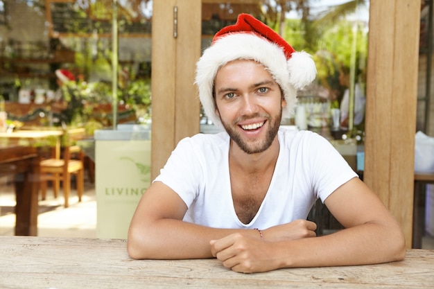 Hübsche stilvolle junge, die Spaß haben, während sie Neujahr auf Firmenfeier feiern, gekleidet wie der Weihnachtsmann, glücklich in die Kamera lächelnd.