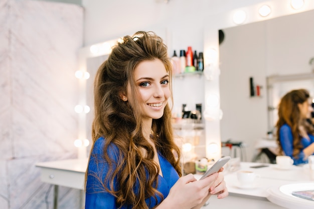 Hübsche süße junge Frau mit langen brünetten Haaren, die zur Kamera im Friseursalon lächeln