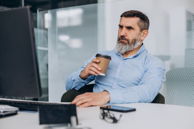 Hübscher älterer Geschäftsmann, der im Büro am Computer arbeitet