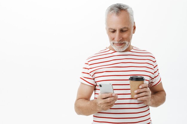 Hübscher älterer Mann, Vater, der Smartphone betrachtet und Kaffee trinkt