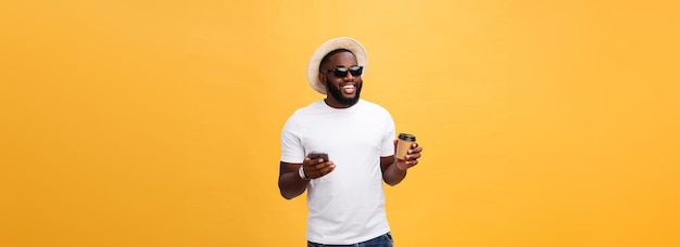 Kostenloses Foto hübscher afroamerikaner mit handy und kaffeetasse zum mitnehmen isoliert über gelbgoldrücken