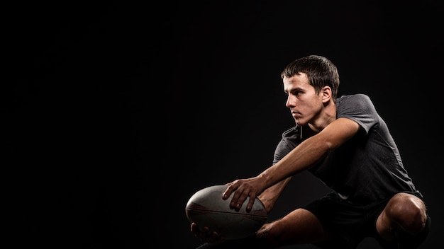 Kostenloses Foto hübscher athletischer männlicher rugbyspieler, der ball mit kopienraum hält