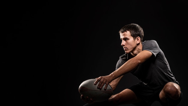 Hübscher athletischer männlicher Rugbyspieler, der Ball mit Kopienraum hält