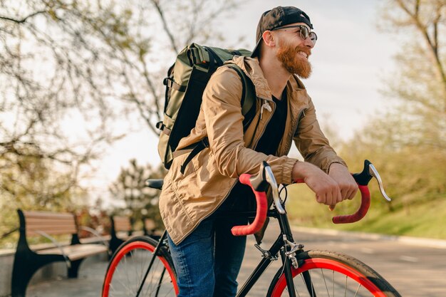 Hübscher bärtiger Mann im Hipster-Stil in Jacke und Sonnenbrille, die allein mit Rucksack auf Fahrrad-Rucksacktourist für gesunden aktiven Lebensstil reiten