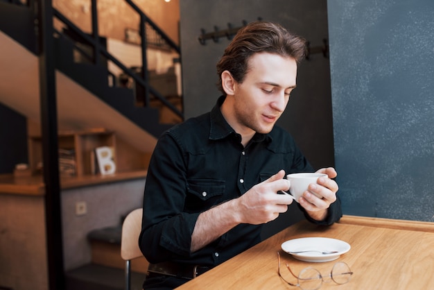 Hübscher bärtiger Mann im karierten Hemd, das Gabel hält, das im Café isst und lächelt