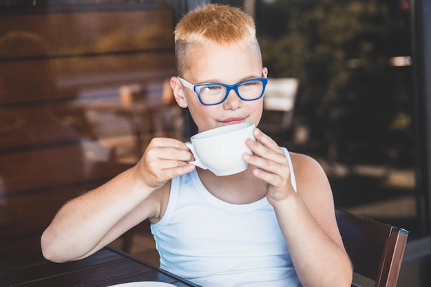 Hübscher blonder junge in einem weißen t-shirt in einem restaurant, das kaffee trinkt