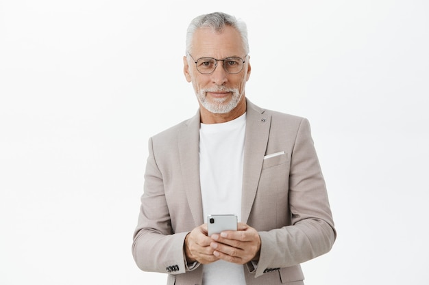 Hübscher erfolgreicher alter Geschäftsmann im Anzug mit Handy