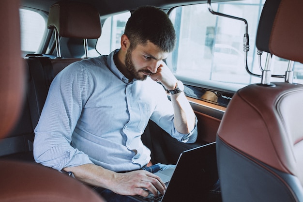 Hübscher Geschäftsmann, der an einem Computer im Auto arbeitet