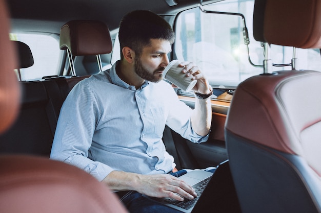 Hübscher Geschäftsmann, der an einem Computer im Auto arbeitet