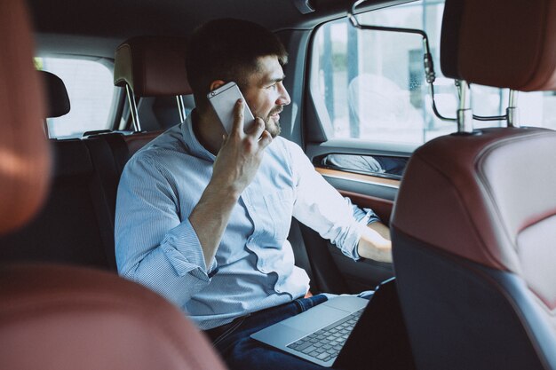 Hübscher Geschäftsmann, der an einem Computer im Auto arbeitet