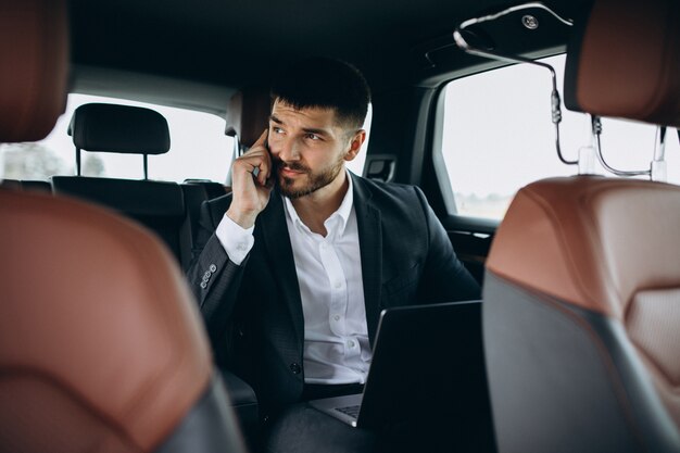 Hübscher Geschäftsmann, der an einem Computer im Auto arbeitet