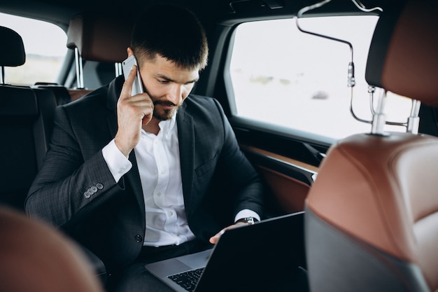 Hübscher Geschäftsmann, der an einem Computer im Auto arbeitet