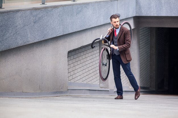 Hübscher Geschäftsmann, der sein Fahrrad auf Stadtstraßen trägt. Das Konzept des modernen Lebensstils junger Männer