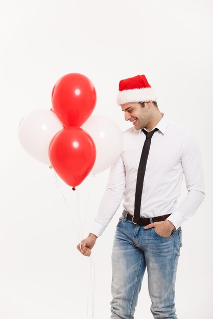 Hübscher glücklicher Geschäftsmann, der mit rotem Ballon geht, feiern frohe Weihnachten, die Weihnachtsmütze tragen.