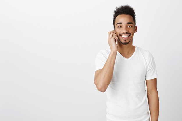 Hübscher glücklicher schwarzer Mann, der lächelt und auf Handy spricht