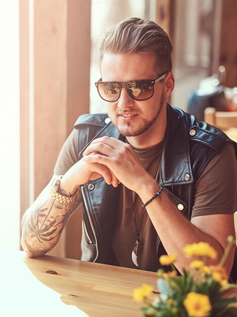 Hübscher Hipster mit stylischem Haarschnitt und Bart sitzt an einem Tisch in einem Straßencafé.