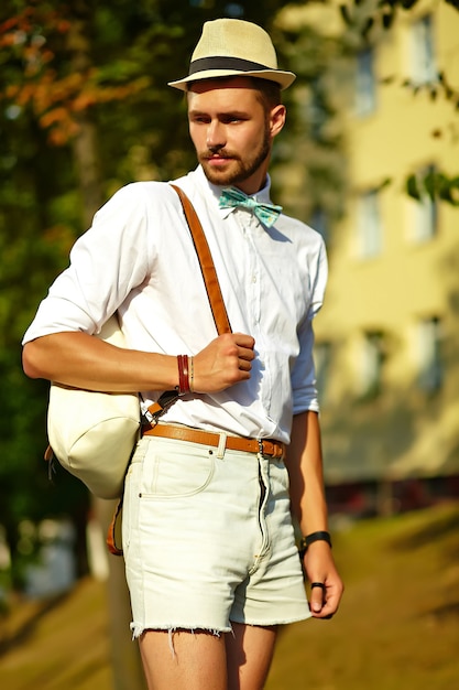 Hübscher Hipster-Modellmann in der stilvollen Sommerkleidung, die im Hut mit Tasche aufwirft