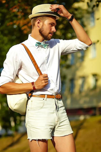 Hübscher Hipster-Modellmann in der stilvollen Sommerkleidung, die im Hut mit Tasche aufwirft