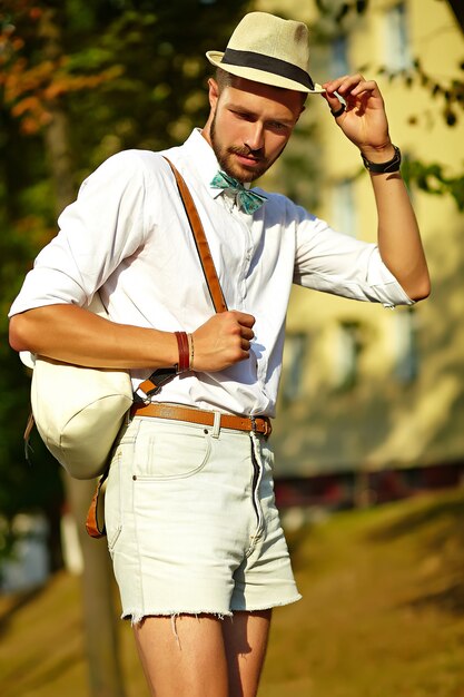 Hübscher Hipster-Modellmann in der stilvollen Sommerkleidung, die im Hut mit Tasche aufwirft