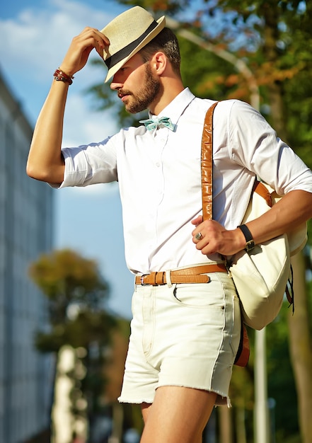 Hübscher Hipster-Modellmann in der stilvollen Sommerkleidung, die im Hut mit Tasche aufwirft