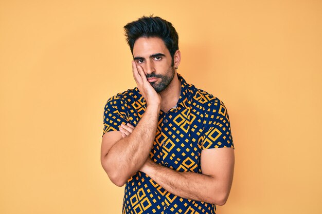 Hübscher hispanischer Mann mit Bart, der ein Hemd im Disco-Stil der 80er Jahre trägt und denkt, er sieht müde und gelangweilt aus, mit Depressionsproblemen und verschränkten Armen.