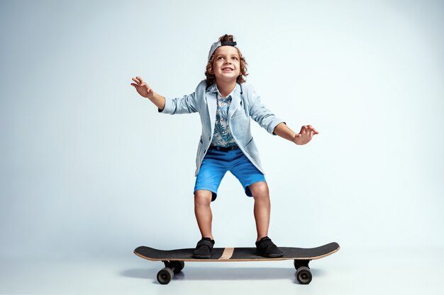 Hübscher Junge auf Skateboard in Freizeitkleidung auf Weiß