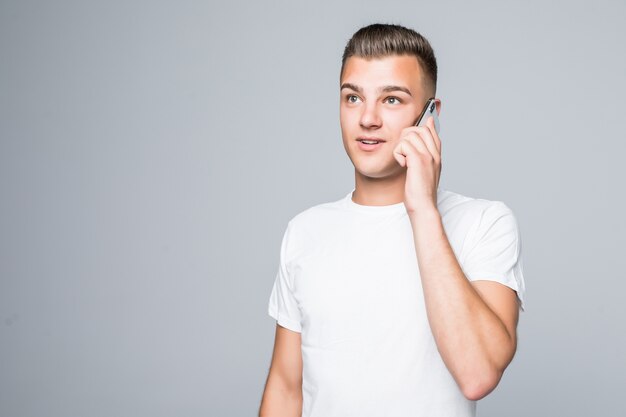 Hübscher Junge im weißen T-Shirt spricht auf seinem Handy isoliert auf weißer Wand