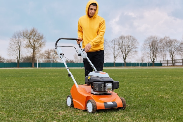 Kostenloses Foto hübscher junger erwachsener männlicher arbeiter, der feld mit grasschneider mäht