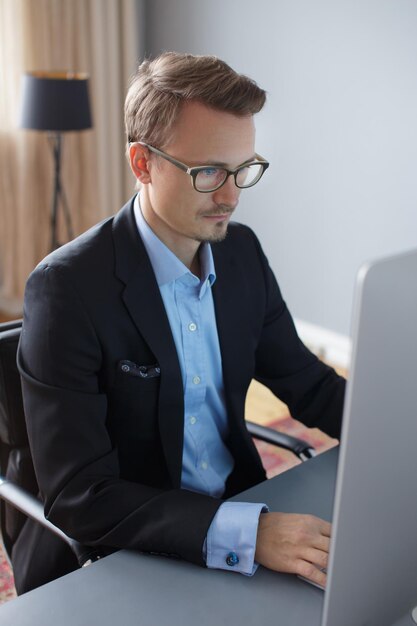 Hübscher junger Geschäftsmann, der mit Computer im Büro arbeitet.