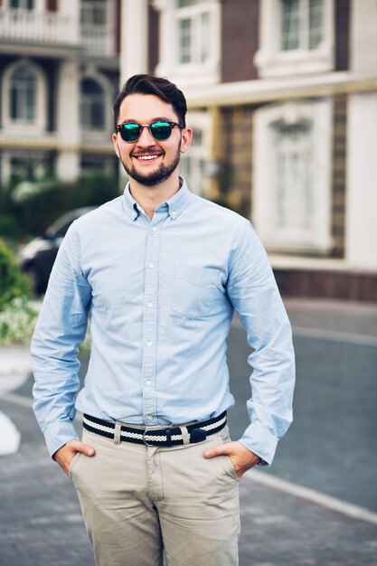 Hübscher junger Geschäftsmann in der Sonnenbrille, die auf Straße geht. Er hält die Hände in den Taschen