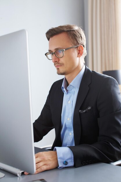 Hübscher junger Geschäftsmann in einem Anzug, der mit Computer im Büro arbeitet.