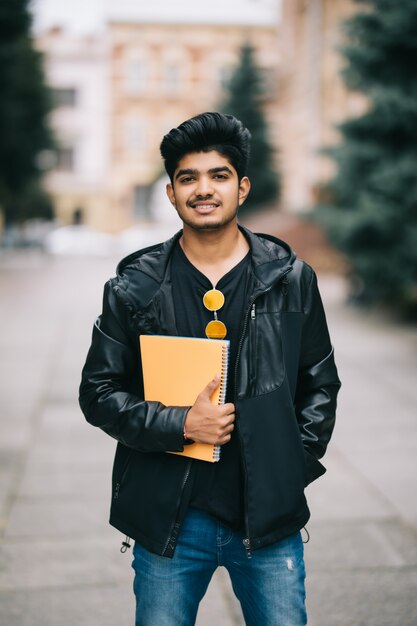 Hübscher junger indischer Studentenmann, der Notizbücher beim Stehen auf der Straße hält