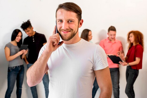 Hübscher junger Mann, der auf Mobiltelefon gegen seine Freunde am Hintergrund spricht