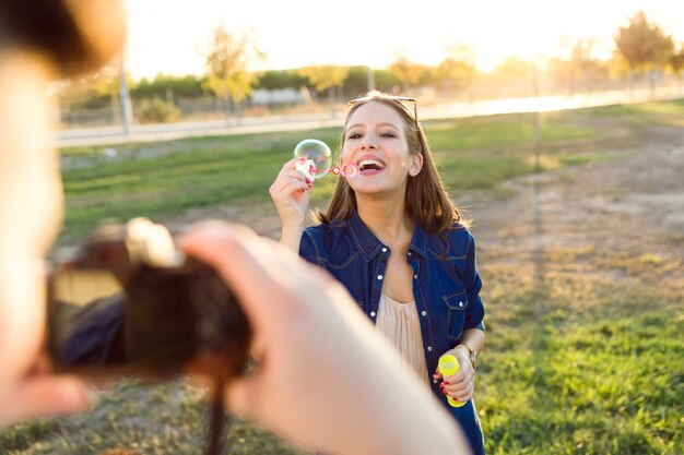 Hübscher junger Mann, der Foto seiner Freundin macht Seifenblasen im Park macht.